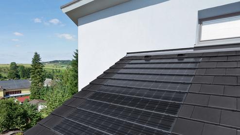 Dach mit schwarzen Solarpanelen über einer ländlichen Umgebung mit Häusern und Bäumen unter blauem Himmel.