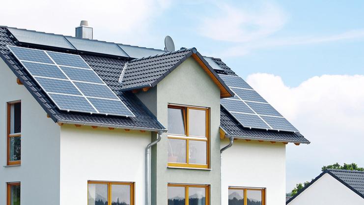 Moderne Neubauvilla mit Solarpanelen auf dem Dach und umgeben von grünem Gras und einem weißen Nebengebäude.